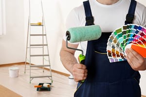 Male decorator with paint roller and color palette samples in empty room, closeup. Space for text